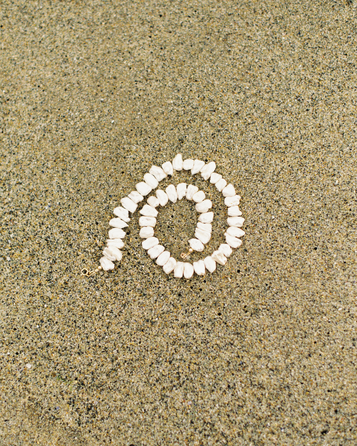 A spiral arrangement of small white shell beads or shells placed on a sandy surface.